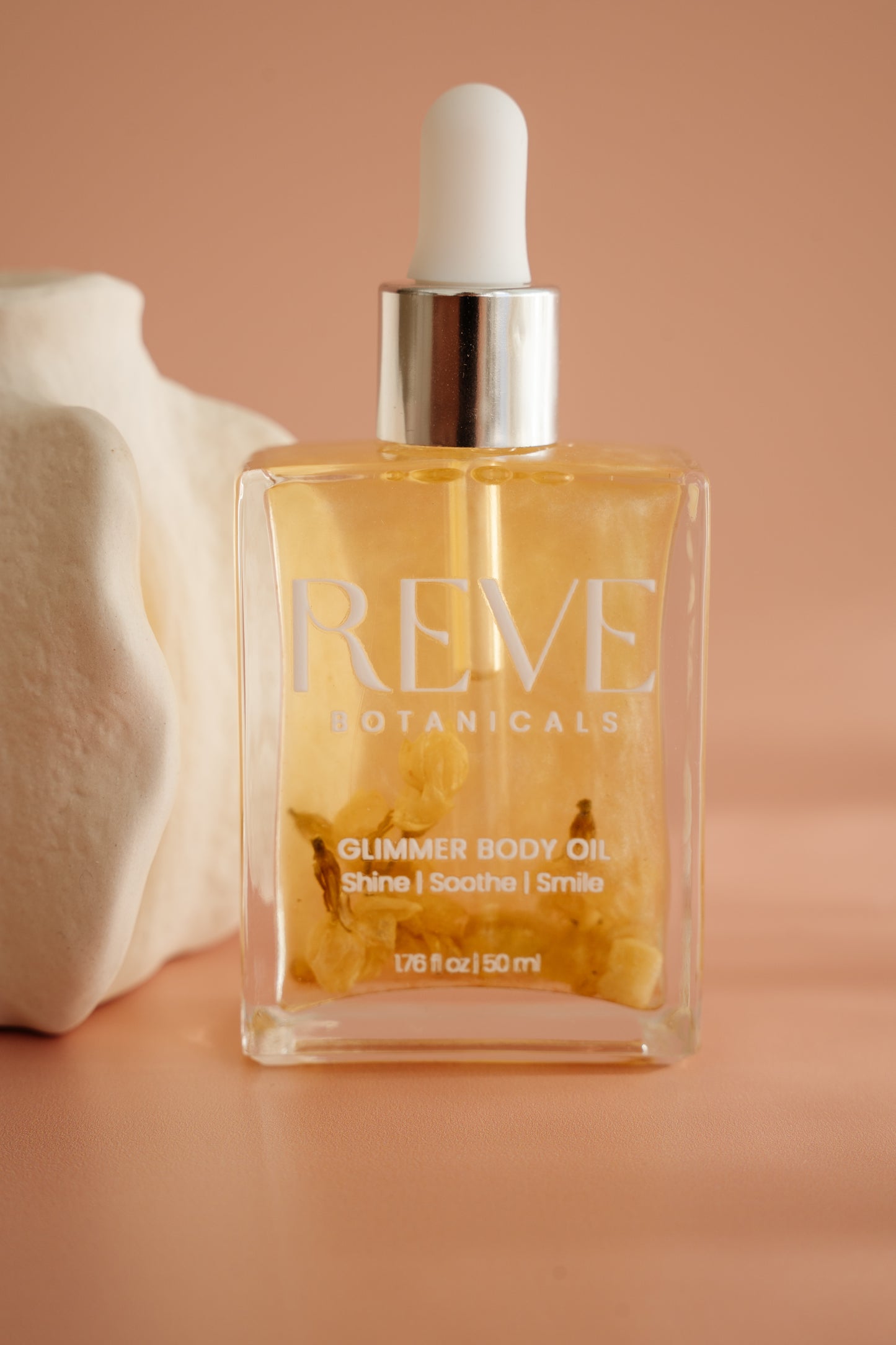 Bottle of Reve Botanicals Glimmer Body Oil on a beige background